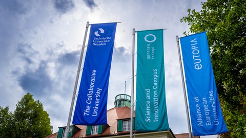 Drei Fahnen vor dem Rektorat der TU Dresden mit den Aufschriften 'The Collaborative University', 'Science and Innovation Campus', 'Alliance of European Universities'.