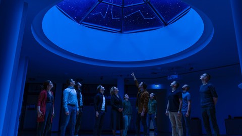 Ein Gruppe von Menschen schaut durch eine Glaskuppel in den Nachthimmel.