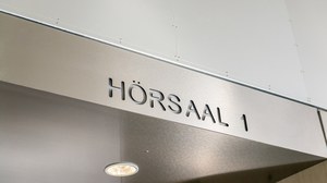 Foto: Abgebildet ist die Inschrift "Hörsaal 1" auf einem silbernen Edelstahlblech.