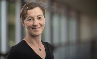 Portrait von Uta Holtzhausen - eine verschmitzt lächelnde Frau mit einer glitzernden Spange im Bob.