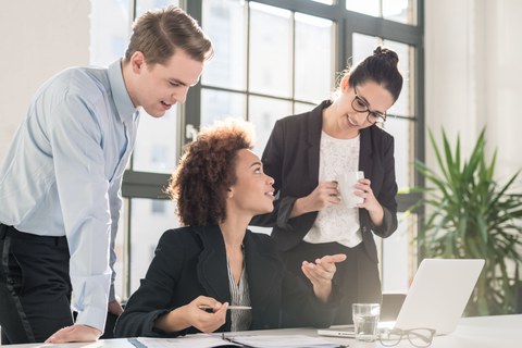 Three persons discuss in front of a computer.