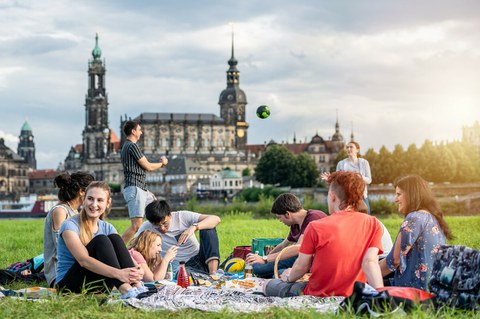 Gruppe von Studenten an der Elbe. Sie spielen Volleyball und sitzen plaudernd auf der Wiese.