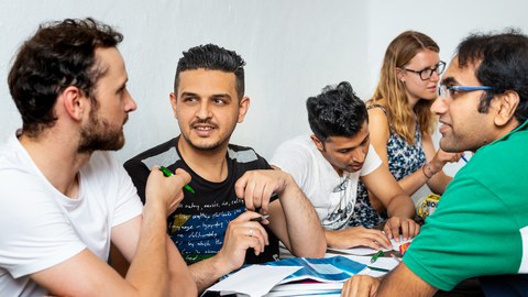 Photo of several people from different countries talking and solving tasks together.