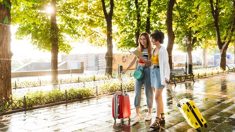 Photo of two people looking at map with suitcases in hand