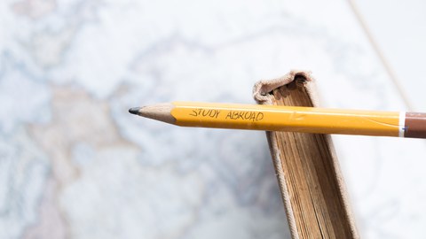 Photo of a pencil with the inscription "Study Abroad". The pencil is on a book and both are on a world map.