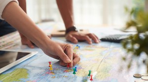 Photo of a world map with a person marking points with pins
