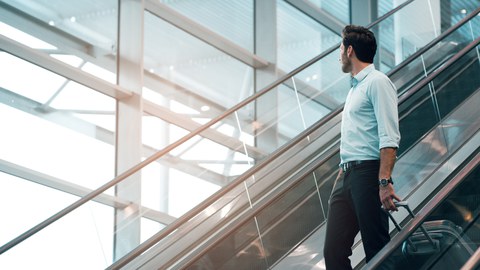 Photo of a person with suitcase on a staircase in a large glass hall