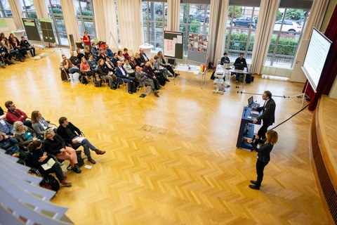 Vortrag. Voller Saal mit Redner und Dolmetscherin für DGS