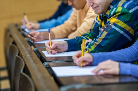 Studierende sitzen im Hörsaal und halten einen Stift in der Hand