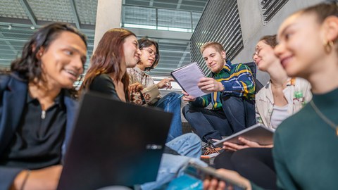 Foto von sechs Studierenden, die auf dem TUD-Campus auf einer Treppe sitzen und zusammen lernen