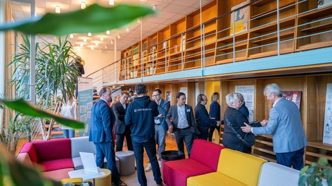 etwa 18 Menschen aus der Gründerszene stehen bei einem Treffen von TUD|excite in kleinen Gesprächsgrüppchen oder schütteln Hände. Im Raum stehen kleine Besprechungssofas, Roll-ups, Bücherregale und Zimmerpflanzen. 