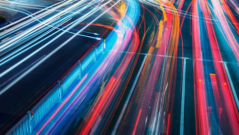 Bunte Verkehrslichter auf einer großen vielbefahrenen Straßenkreuzung in Zeitraffer bei Nacht.