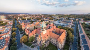 The photo shows an aerial view of the Georg Schumann Building at the TU Dresden. The building looks like a kind of castle. The large fortified tower and the pointed roofs are particularly striking.