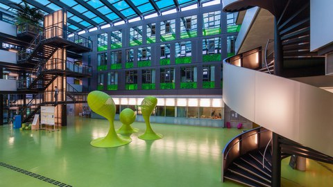 Das Foto zeigt das Foyer des Andreas-Pfitzmann-Baus der TU Dresden. Der Boden des Foyers ist grün. In der Mitte stehen drei grüne Skulpturen. 