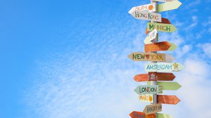 The photo shows a signpost against a blue sky with a few small clouds. There are arrows on the signpost. They bear the names of large cities and point in the direction in which the cities are located.