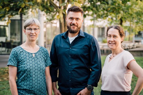 group picture of three people smiling standing outside in the green environment