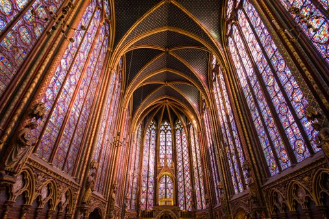 Inside view of a church with large, delicate stained glass windows on all sides, covered by a Gothic vaulted ceiling.