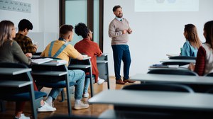 Foto: In einem Seminarraum steht ein Dozierender vor mehreren Zuhörer:innen.