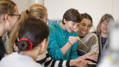 Junge Frauen stehen im Halbkreis und tropfen mit einer Pipette auf einen Objektträger