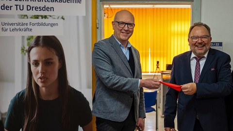 Zwei Männer stehen vor einer geöffneten Tür und halten ein Stück rotes Band in der Hand