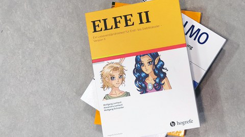 ELFE-material on top of a stack of folders containing research materials. On a yellow background is the title “ELFE 2. A reading comprehension test,” and below it, on a white background, are two manga-style comic characters.