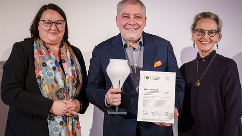 Katrin Stump (left) and Prof. Ursula Staudinger (right) present the certificate and vessel statuette to top chef Christian Bau.