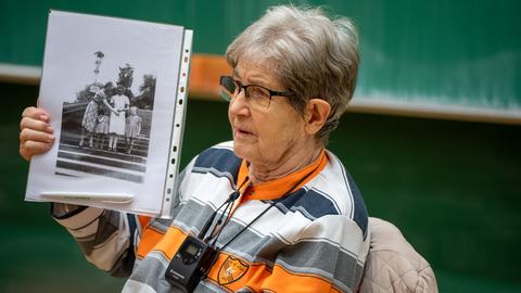 Renate Aris hält ein Schwarzweißfoto von sich in die Luft