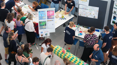 Foto von mehreren Personen bei der Langen Nacht der Wissenschaft an einem Stand mit verschiedenen Plakaten und Modellen
