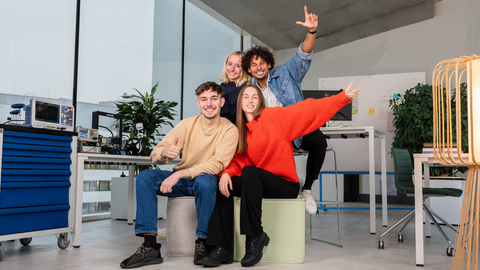 Gruppe junger Leute die in einem Bürogebäude lächelnd in die Kamera schauen.