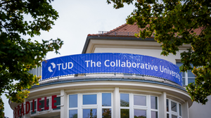Photo of a blue TUD banner with the TUD logo and white lettering reading “The Collaborative University” at the crosswalk.